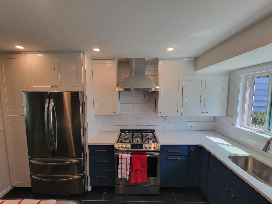 Modern kitchen with stainless steel appliances, white and blue cabinets, and white countertops.
