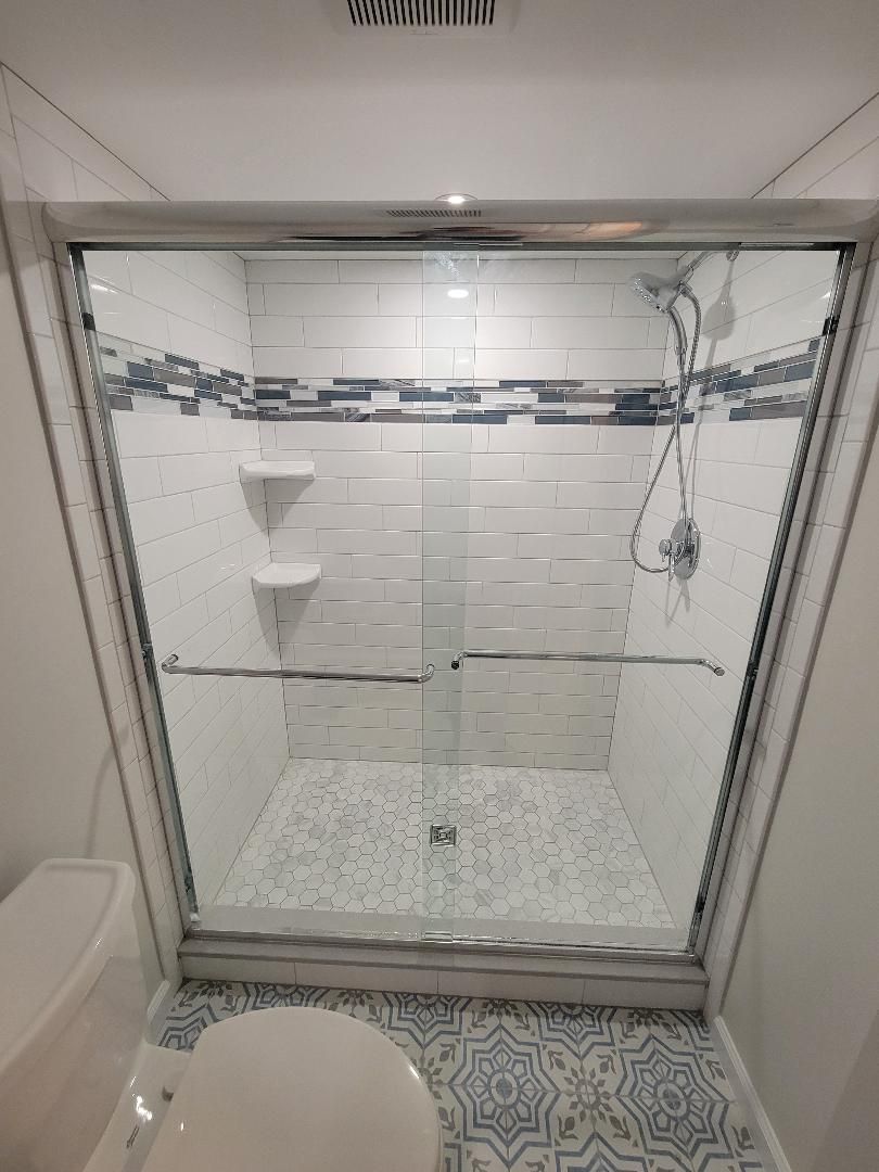 Shower with glass doors, white and blue tiled walls and floor, and a toilet.