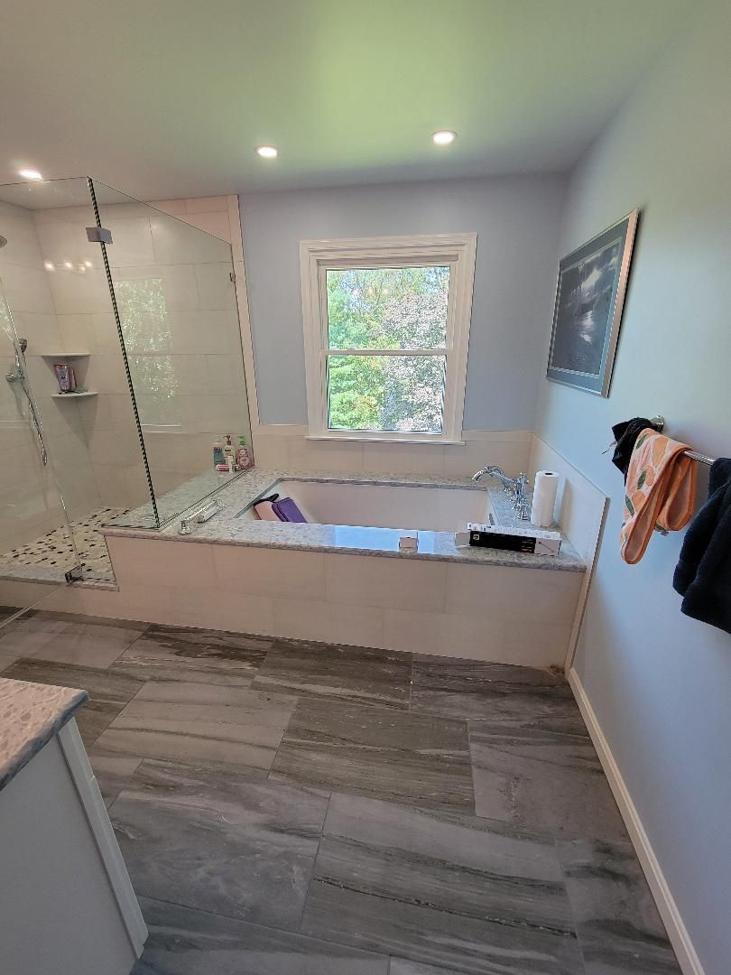 Bathroom with tub, glass shower, light blue walls, grey tile floor, and window.