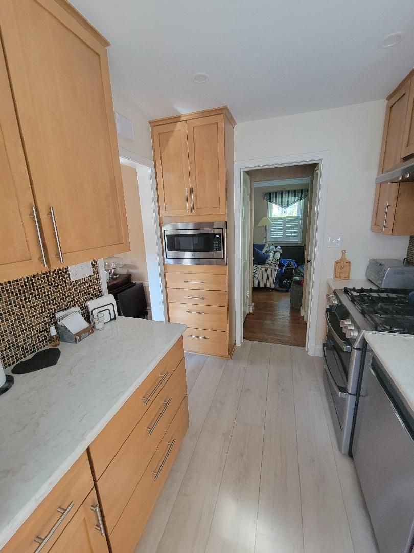 Kitchen with light wood cabinets, white countertops, and a view into a hallway.