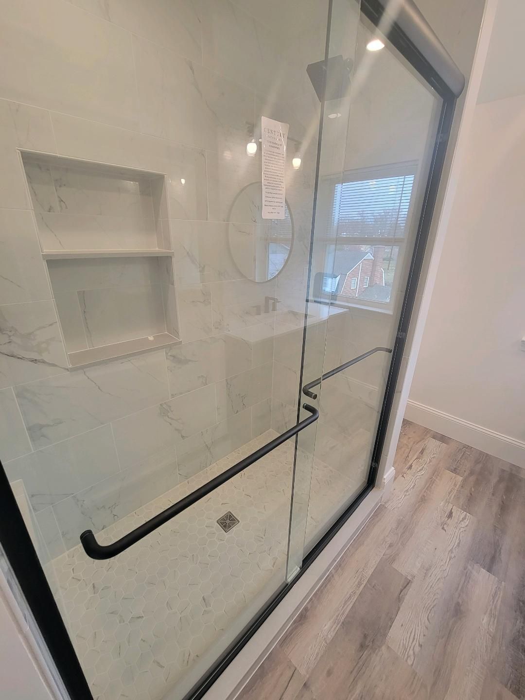Modern bathroom with a glass shower, black trim, and white marble tile.