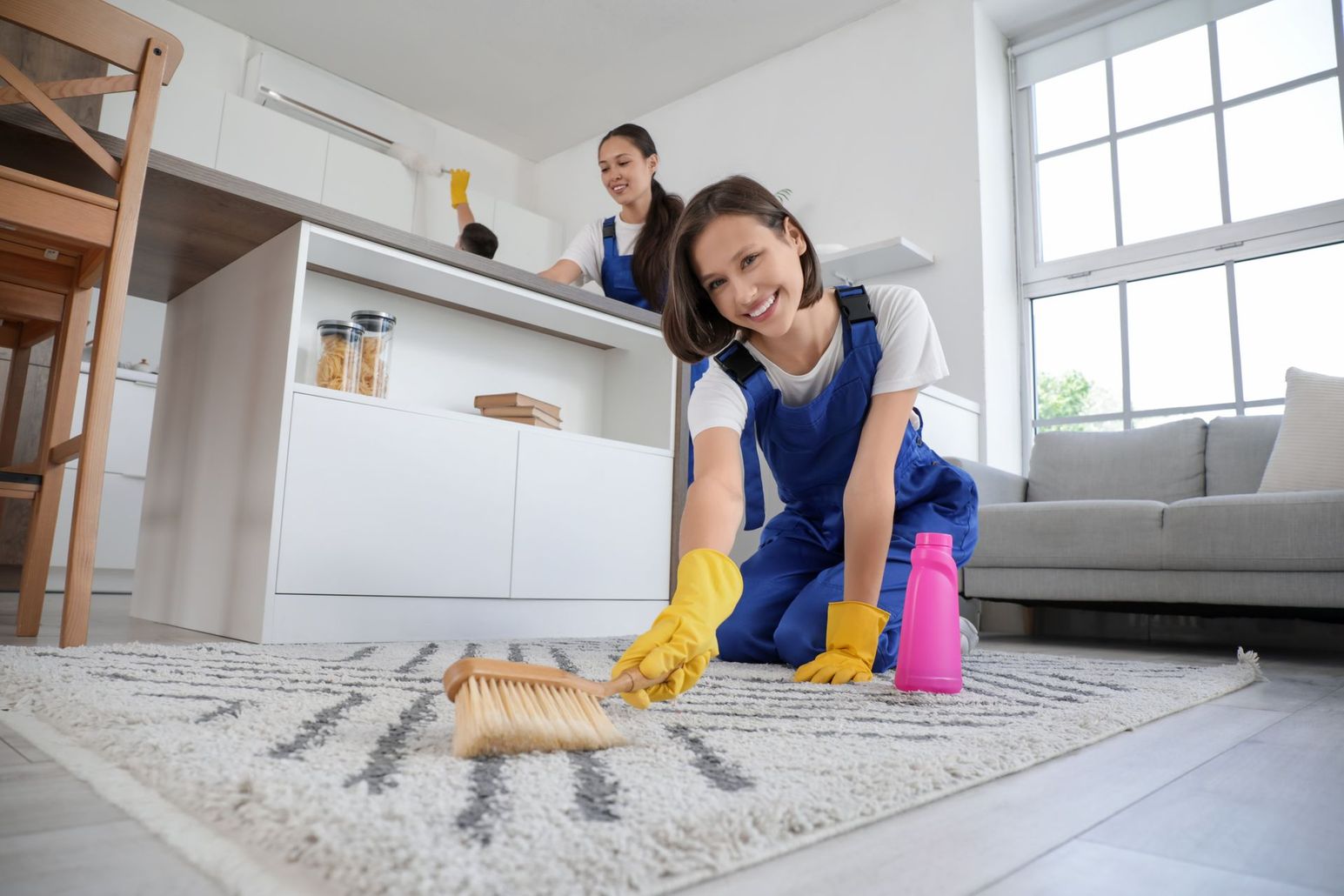 Two women are cleaning a rug in a living room.