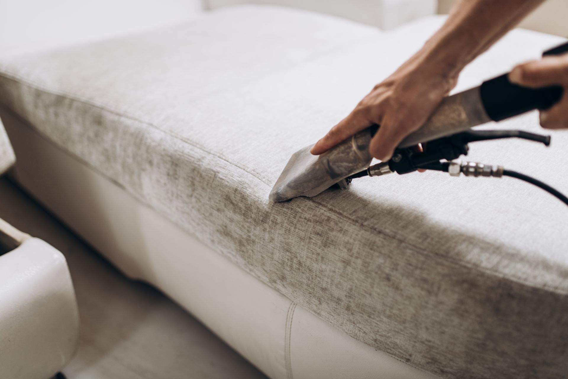 A person is cleaning a couch with a vacuum cleaner.