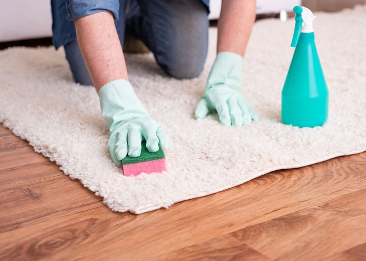 A person is cleaning a rug with a sponge and spray bottle.