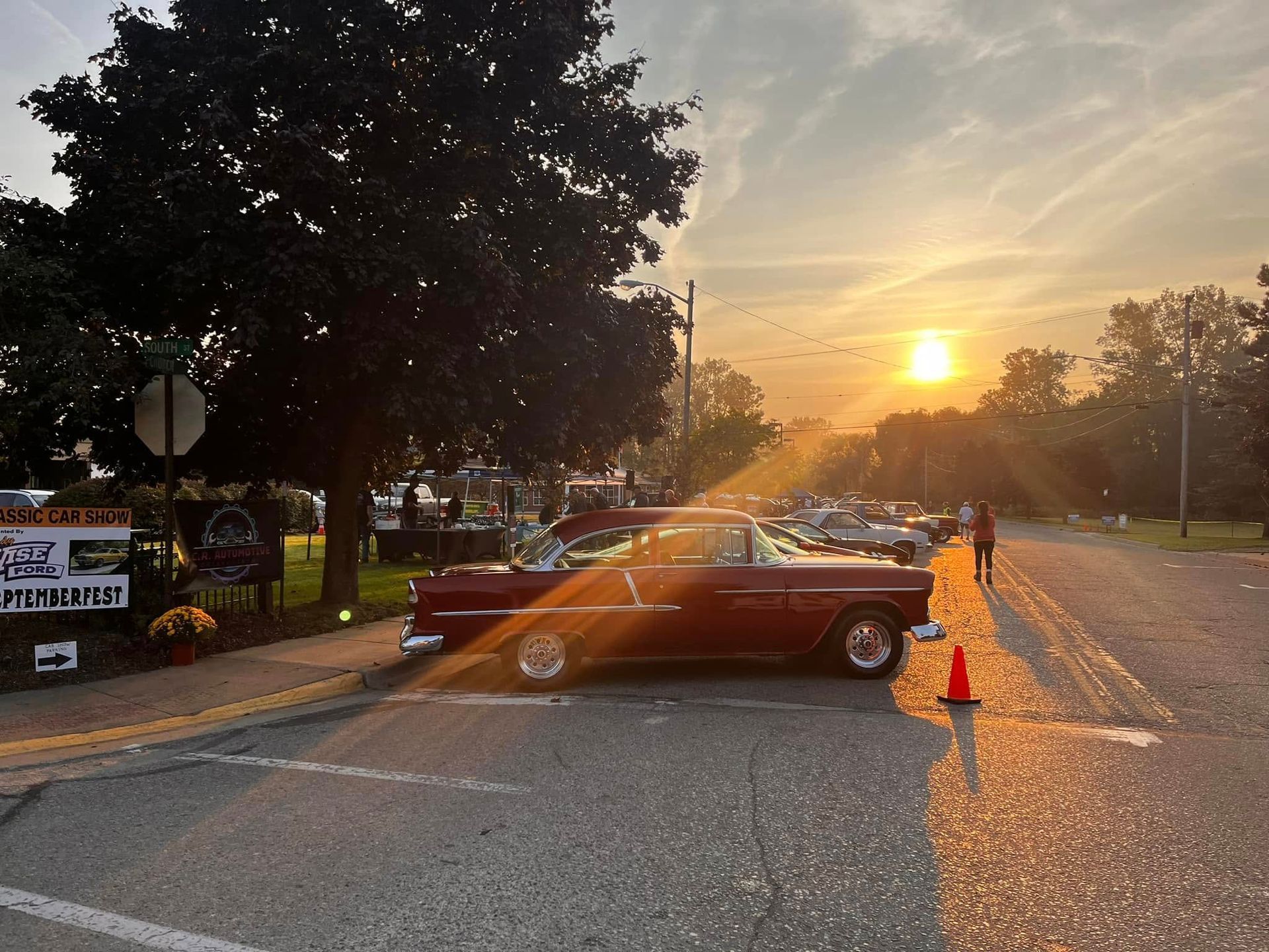 Classic red car at a car show, with the sunset behind it.