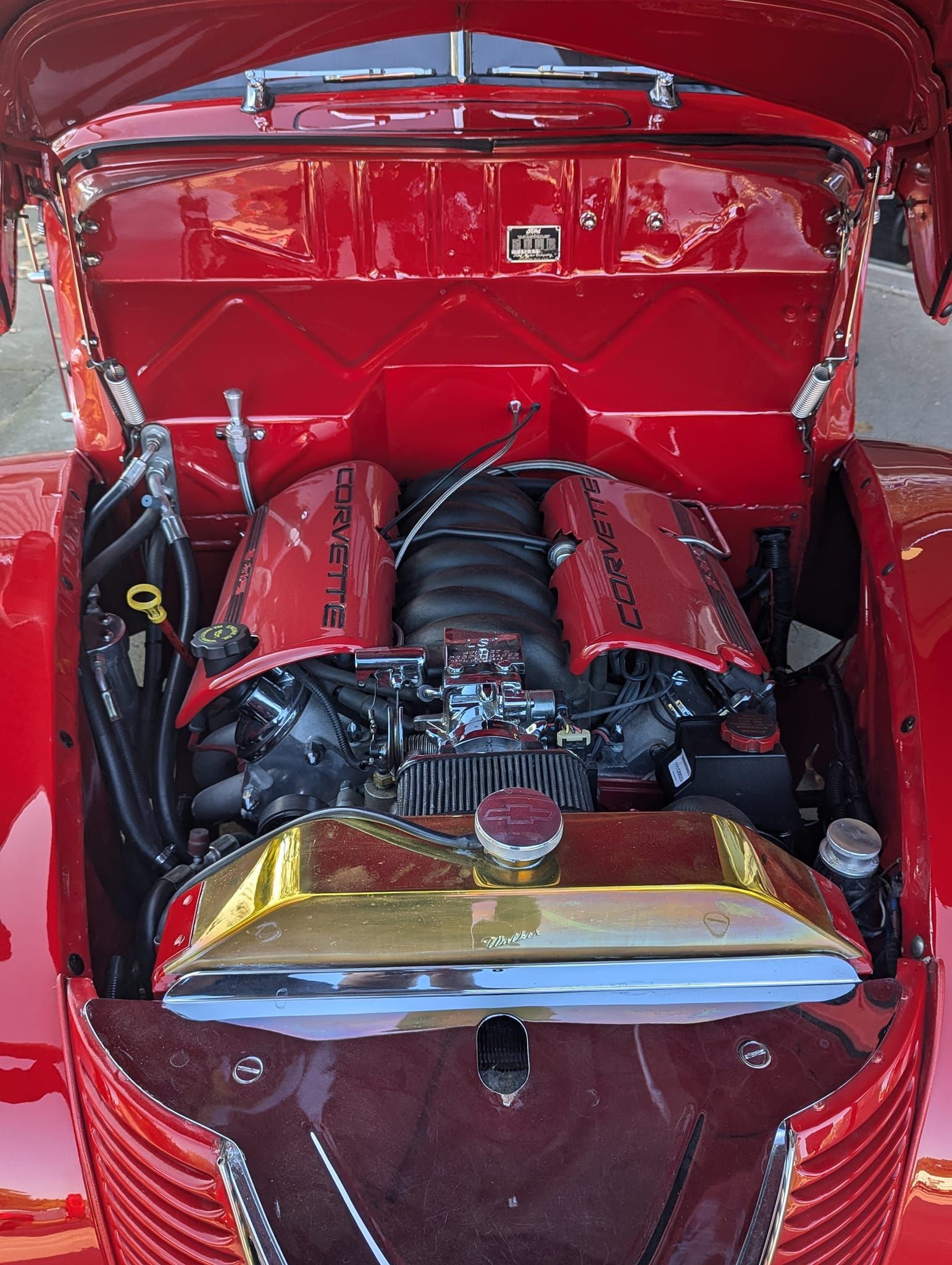 Red classic car engine bay, featuring a modern engine, gold radiator, and custom covers.