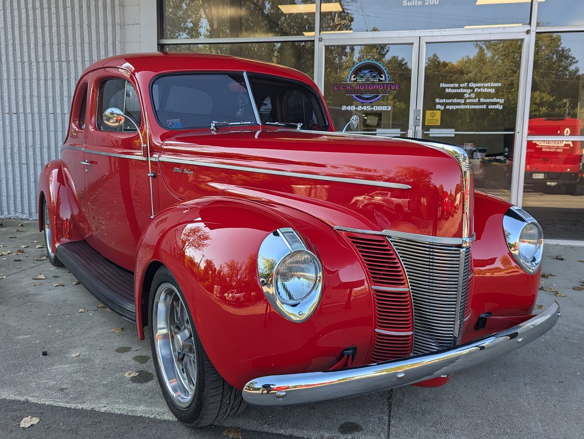 Red 1940 Ford coupe parked in front of a storefront. Chrome grill, headlights and bumper.