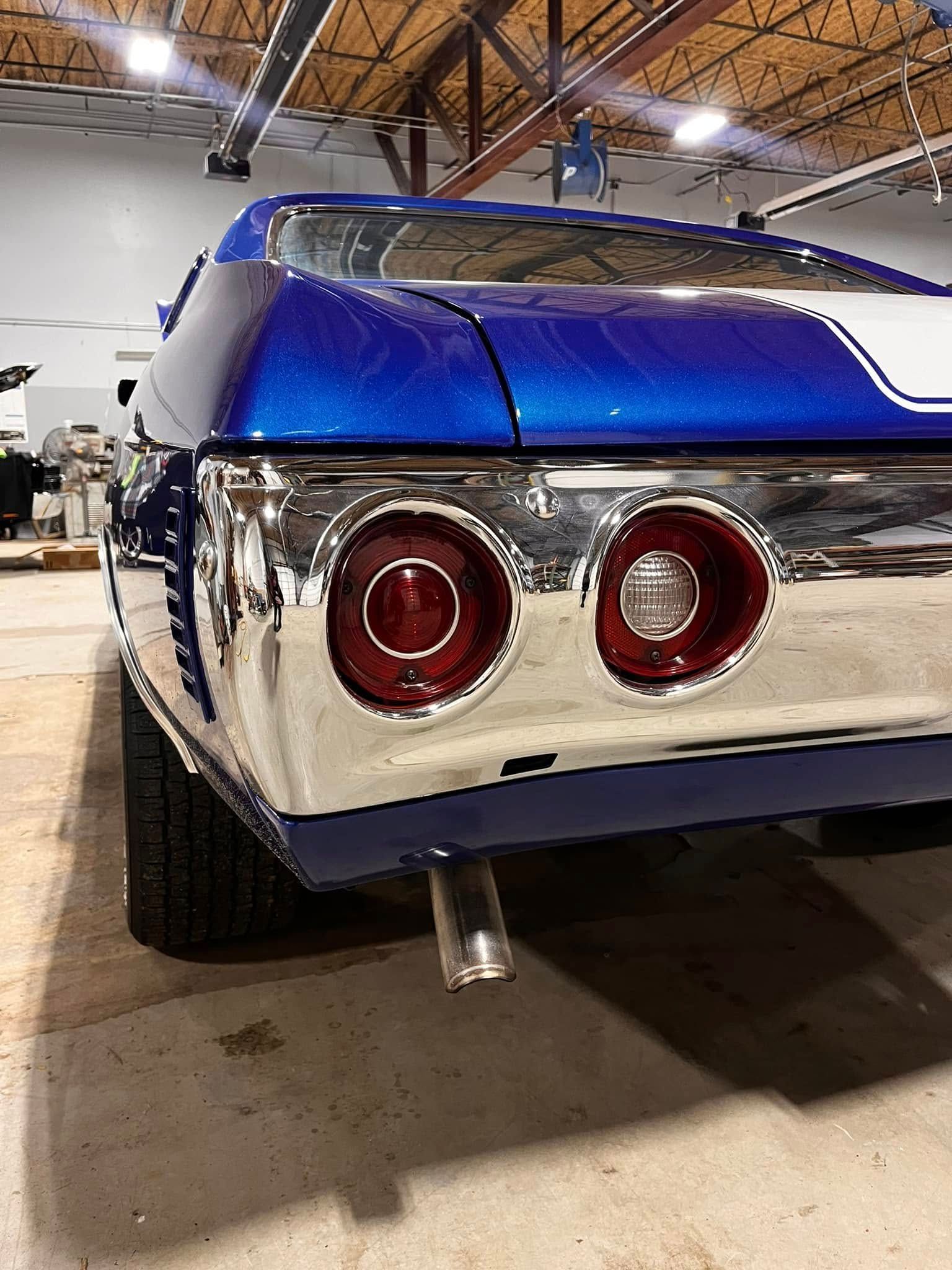 Blue and chrome classic car, rear view, white stripe, red taillights, exhaust pipe, indoor.