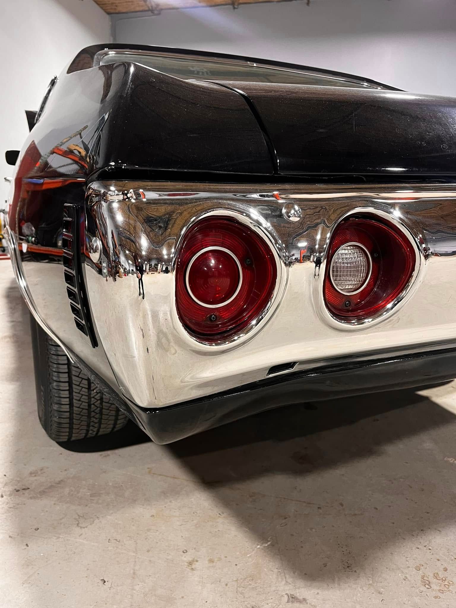 Rear view of a black classic car with chrome details and round red taillights.