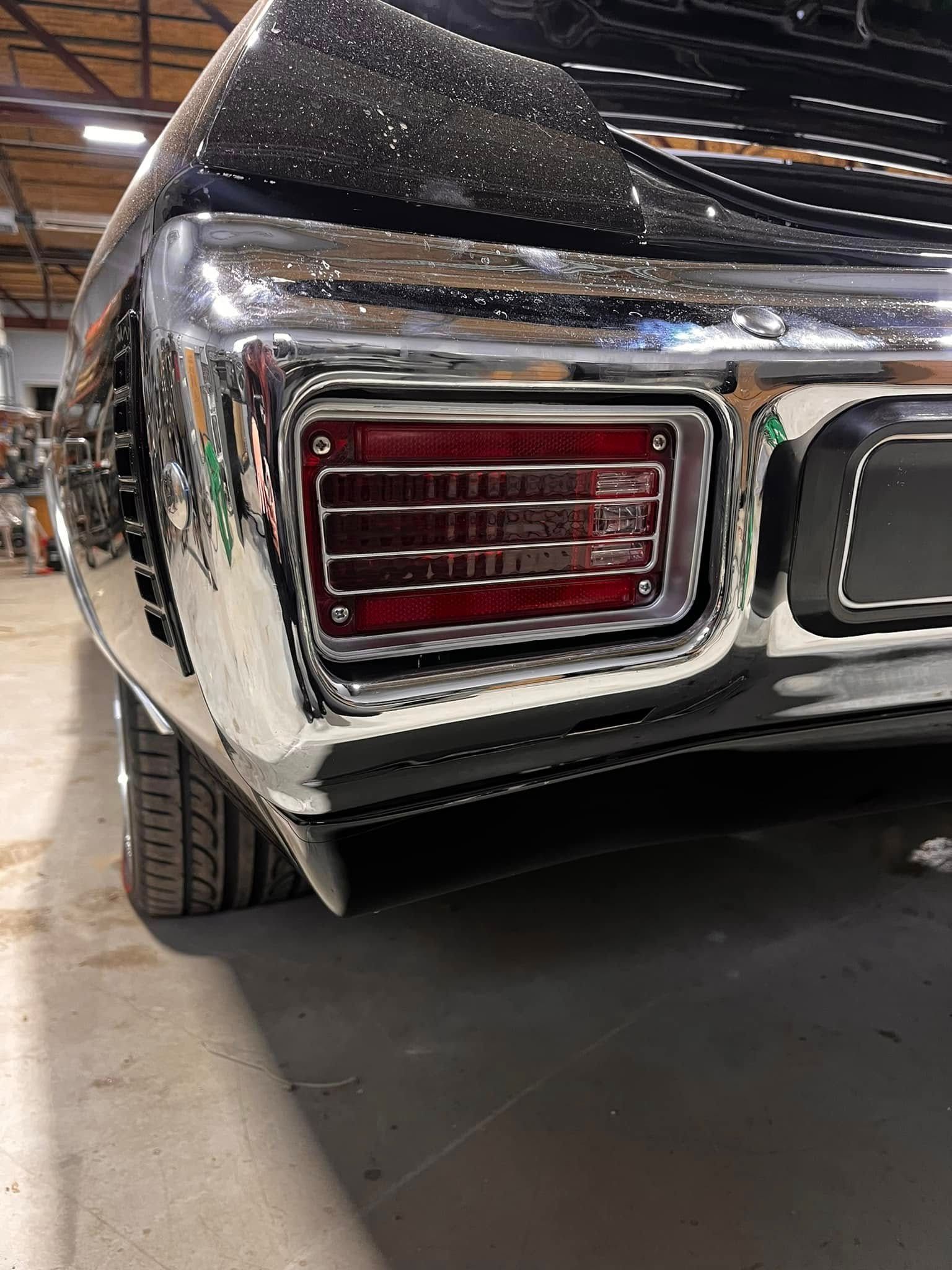 Rear chrome bumper and taillight of a black classic car. The taillight is red.