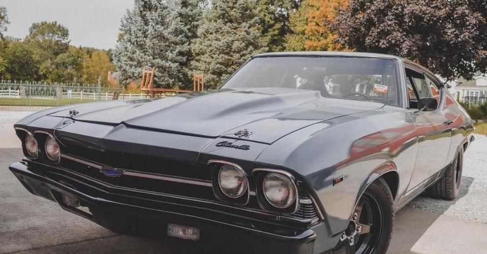 Gray Chevrolet Chevelle muscle car parked in front of a house on a sunny day.
