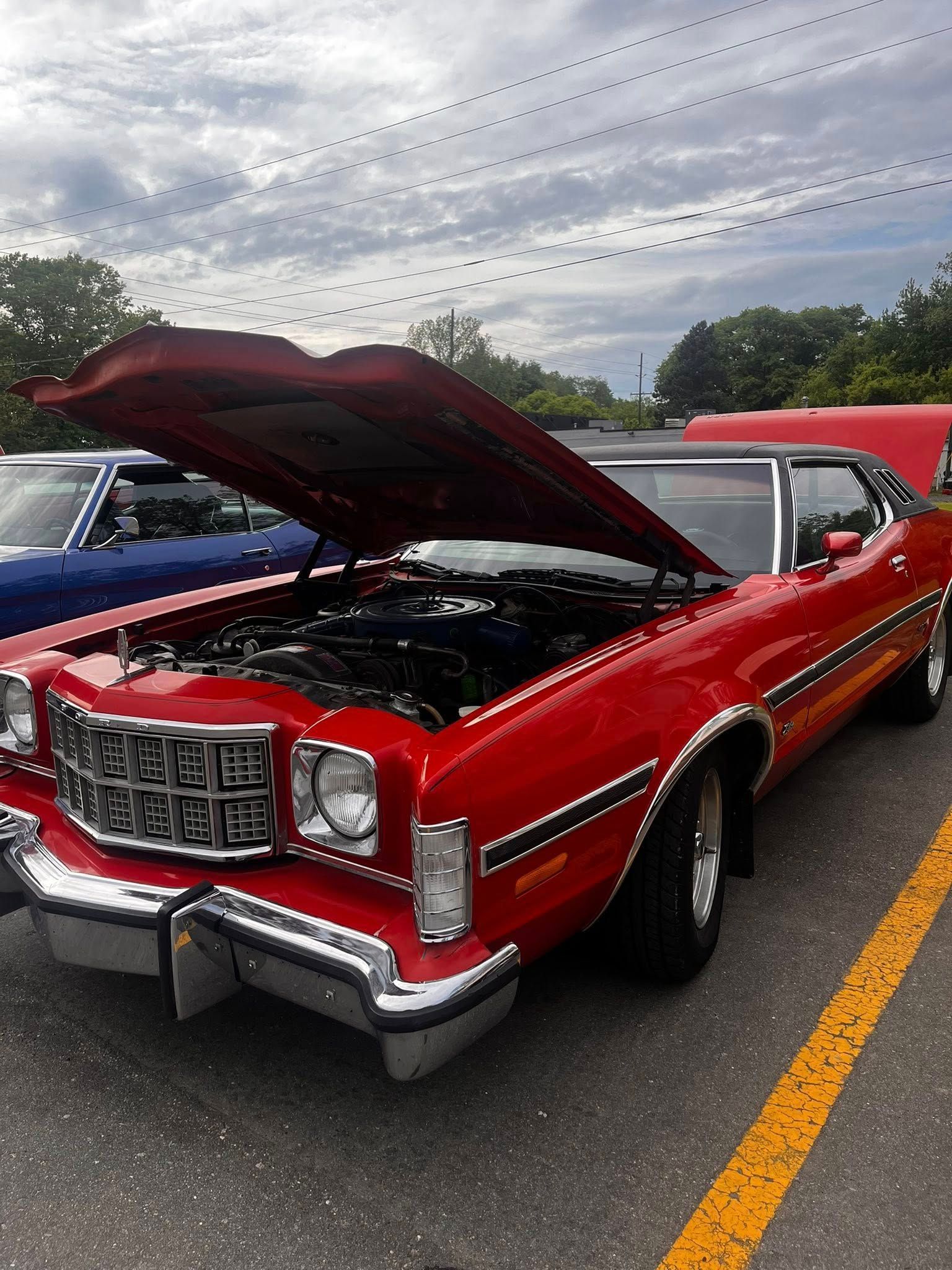 Red classic car with hood open in a parking lot.