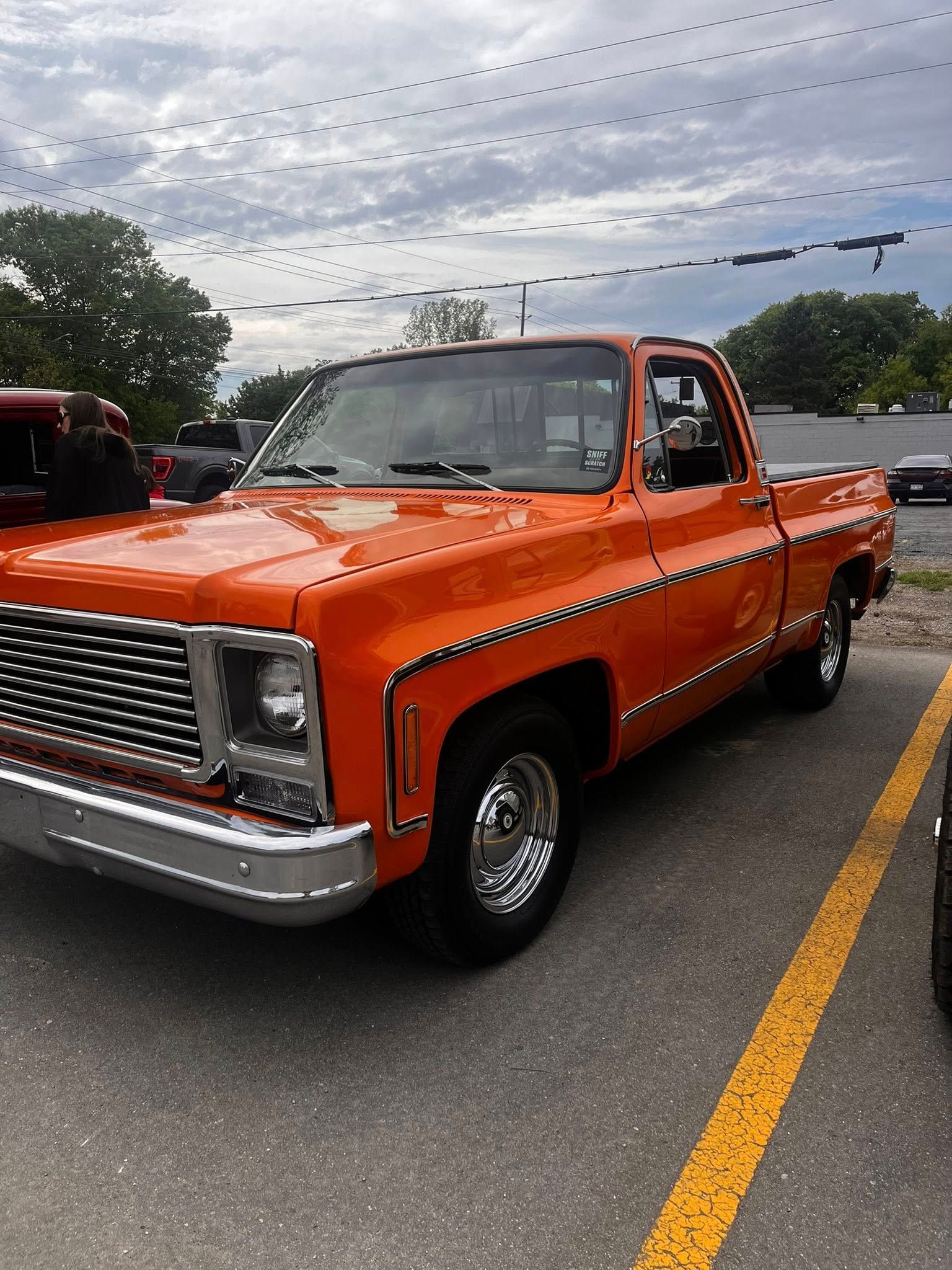 Bright orange classic Chevrolet pickup truck parked in a lot, chrome accents.