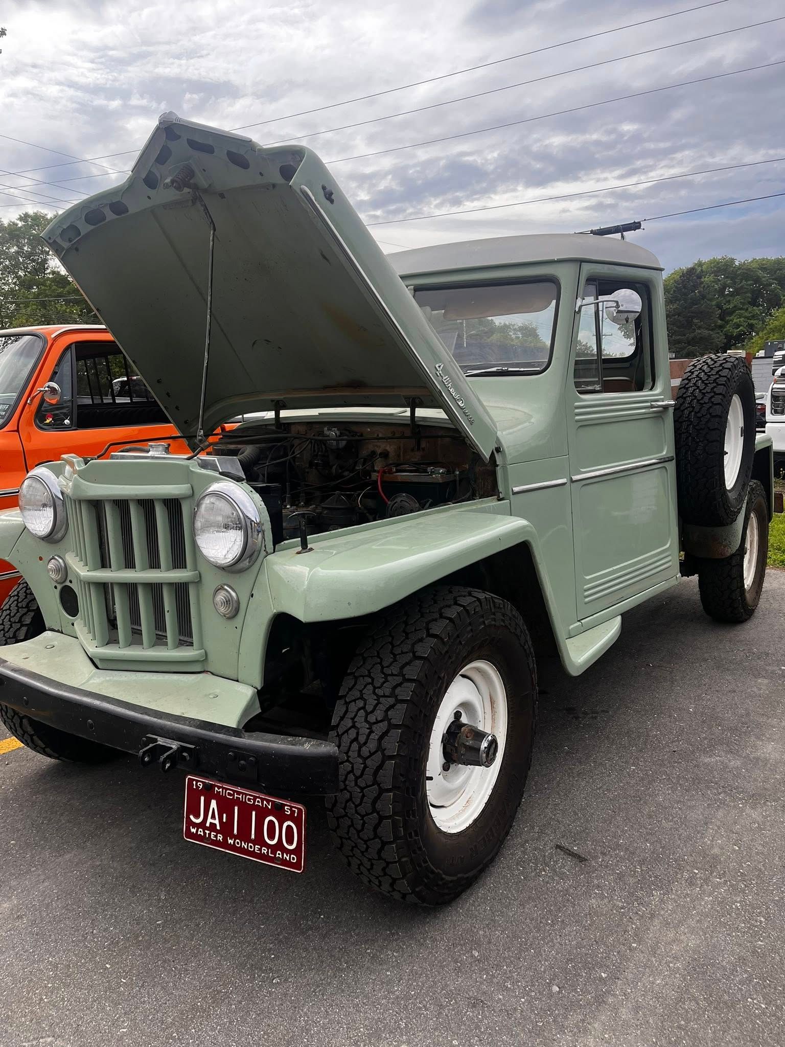 Green vintage Jeep with its hood up, parked outdoors.