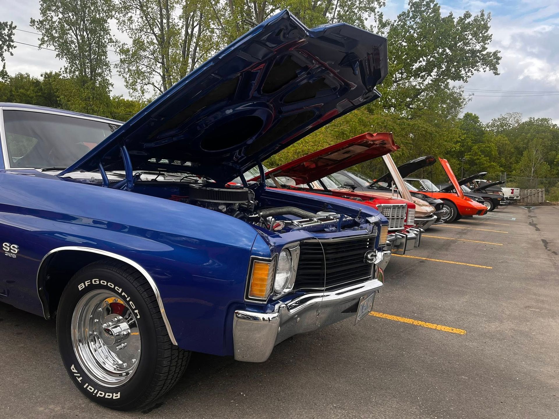 Row of classic cars with hoods open, parked outdoors; blue car in foreground.