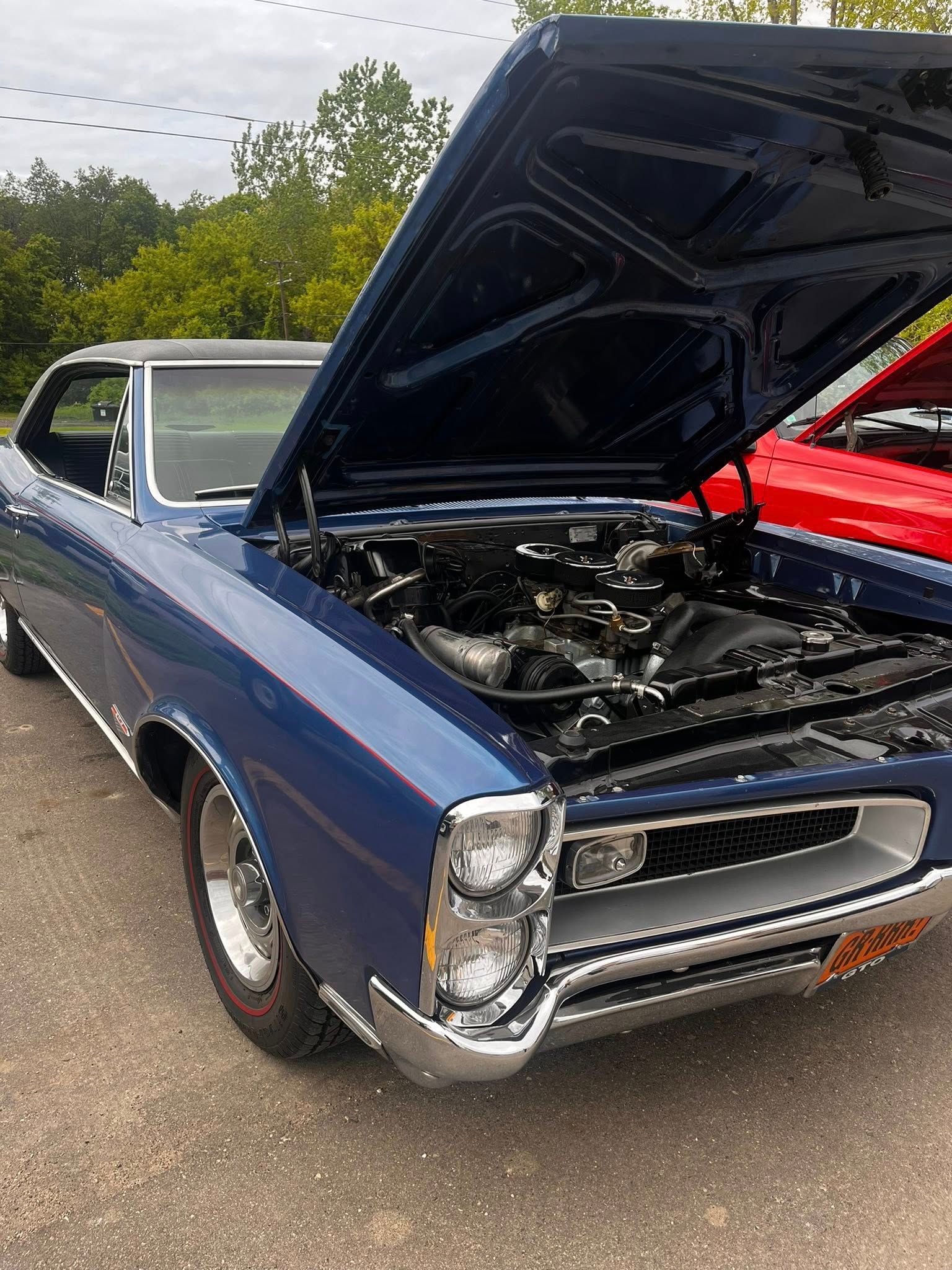 Blue classic car with hood open, showing engine. Parked outdoors.