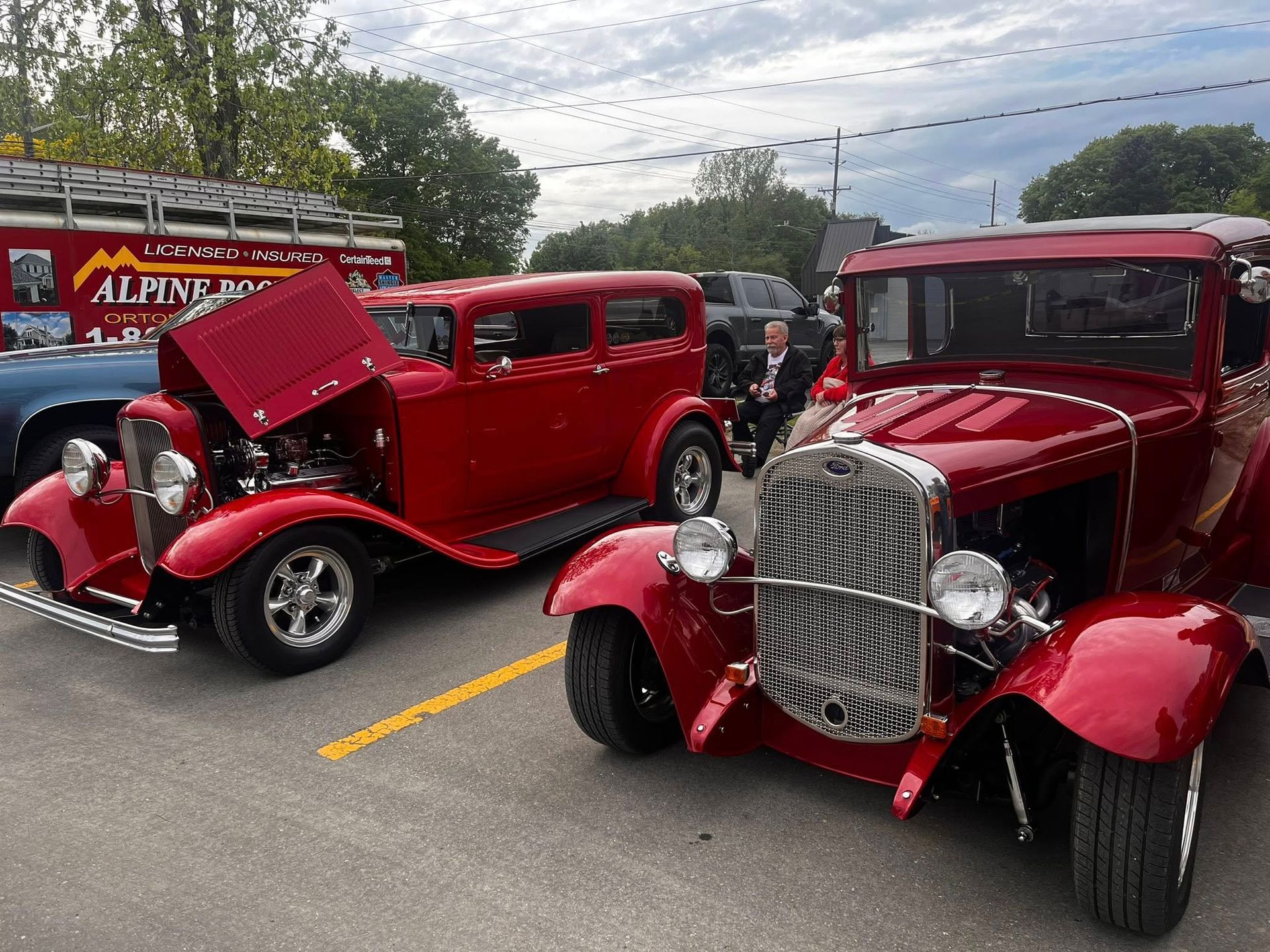Two red classic cars parked outdoors. One has an open hood.