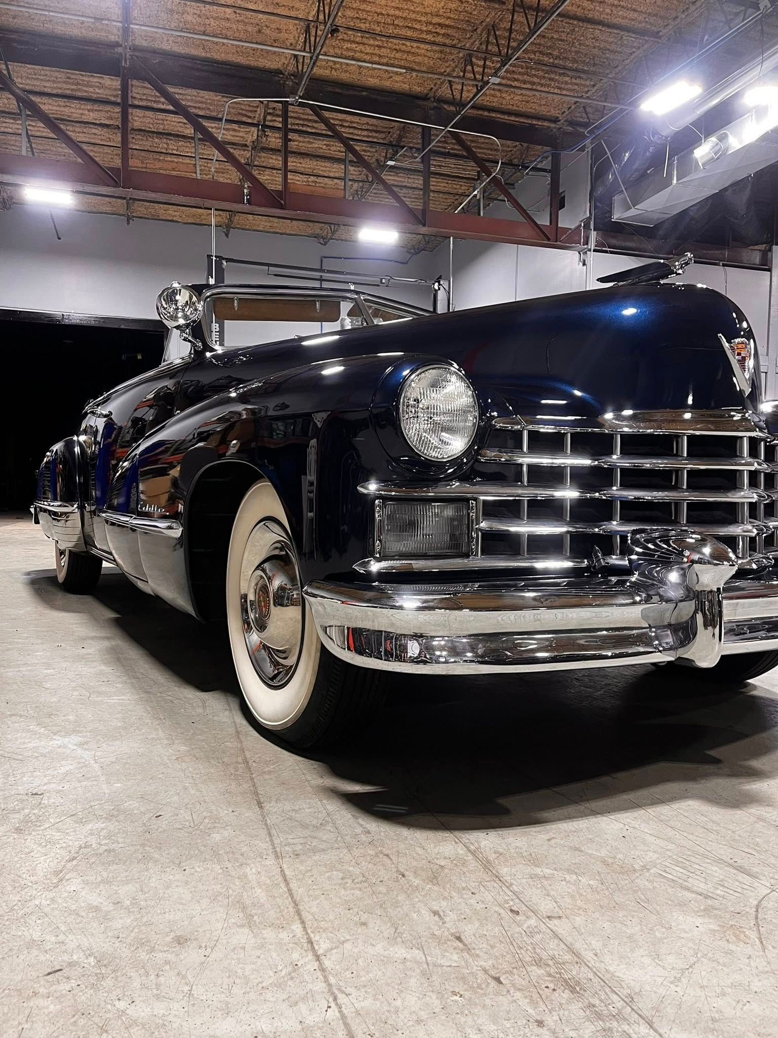 A dark blue vintage Cadillac convertible with whitewall tires parked inside a garage.