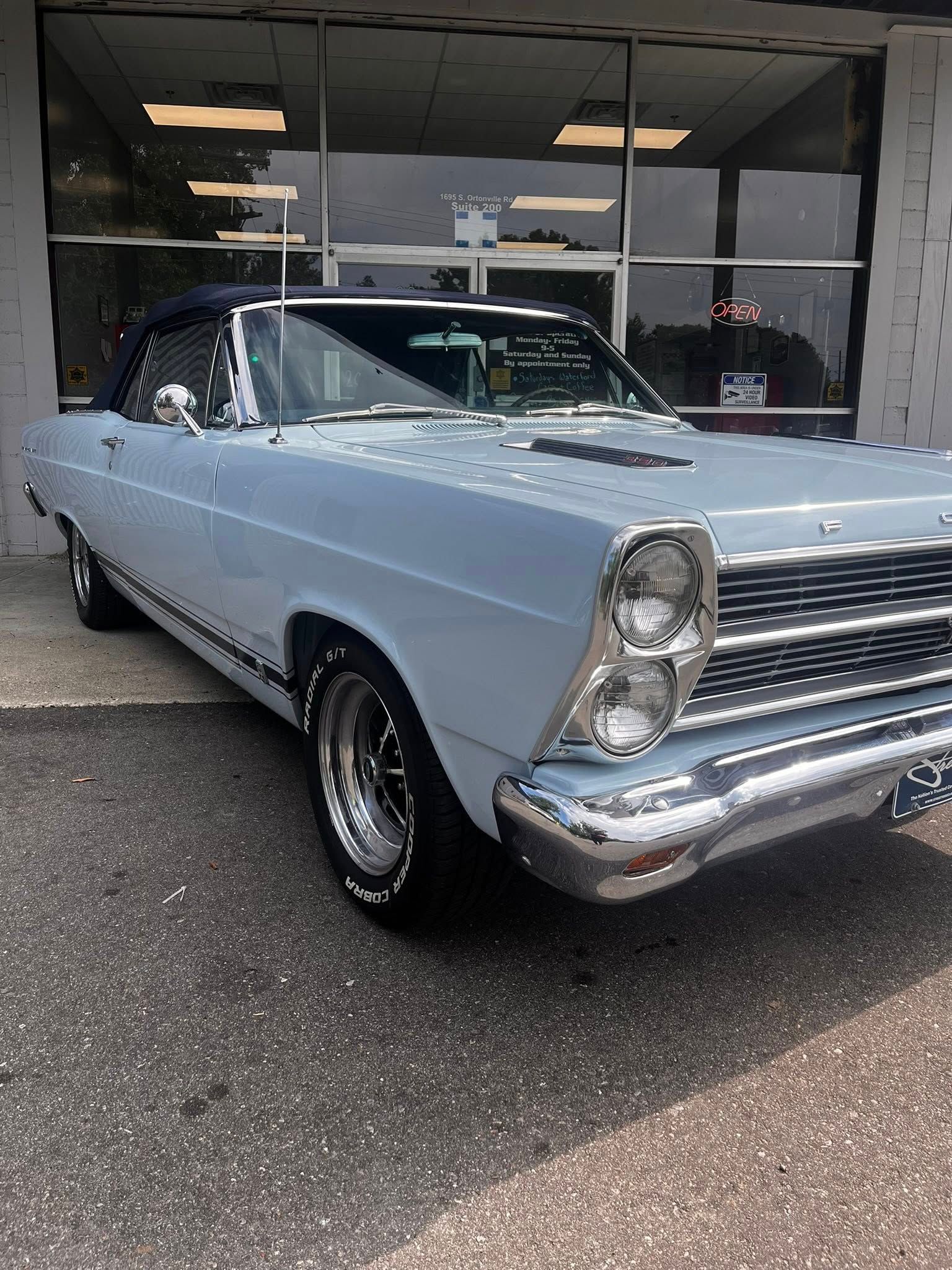 Light blue convertible car parked in front of a building with glass windows.