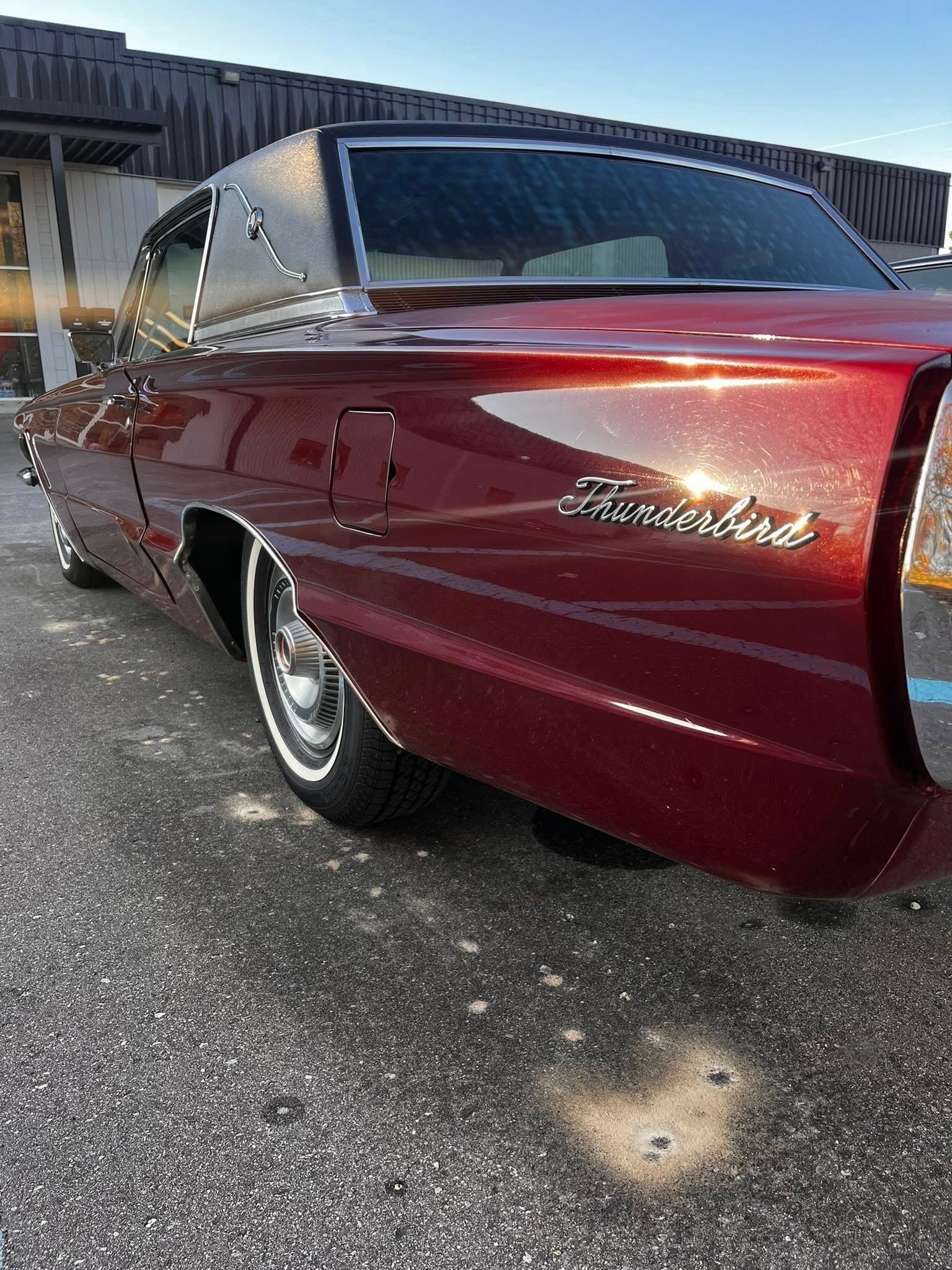 Dark red 1966 Ford Thunderbird with chrome trim and white-walled tires parked on asphalt.