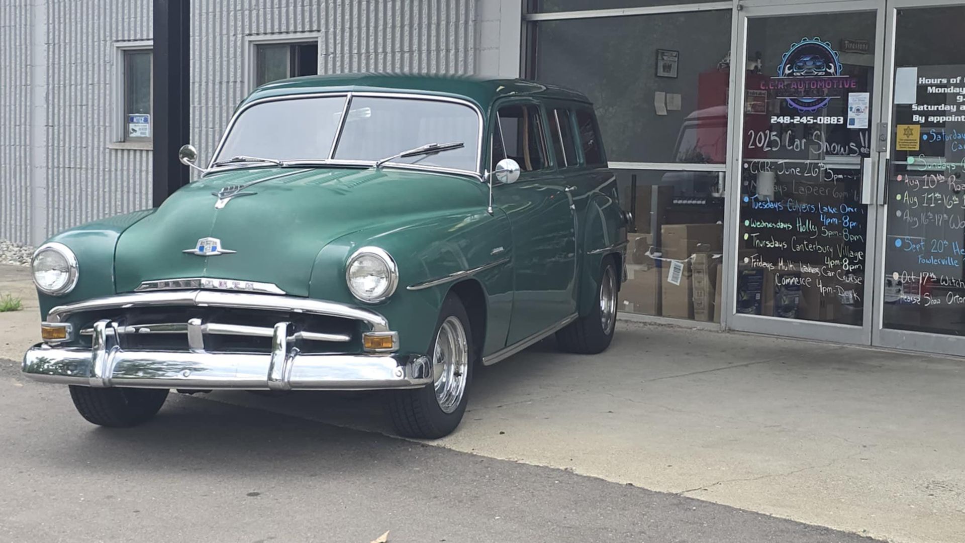 Green vintage station wagon parked outside a store entrance.