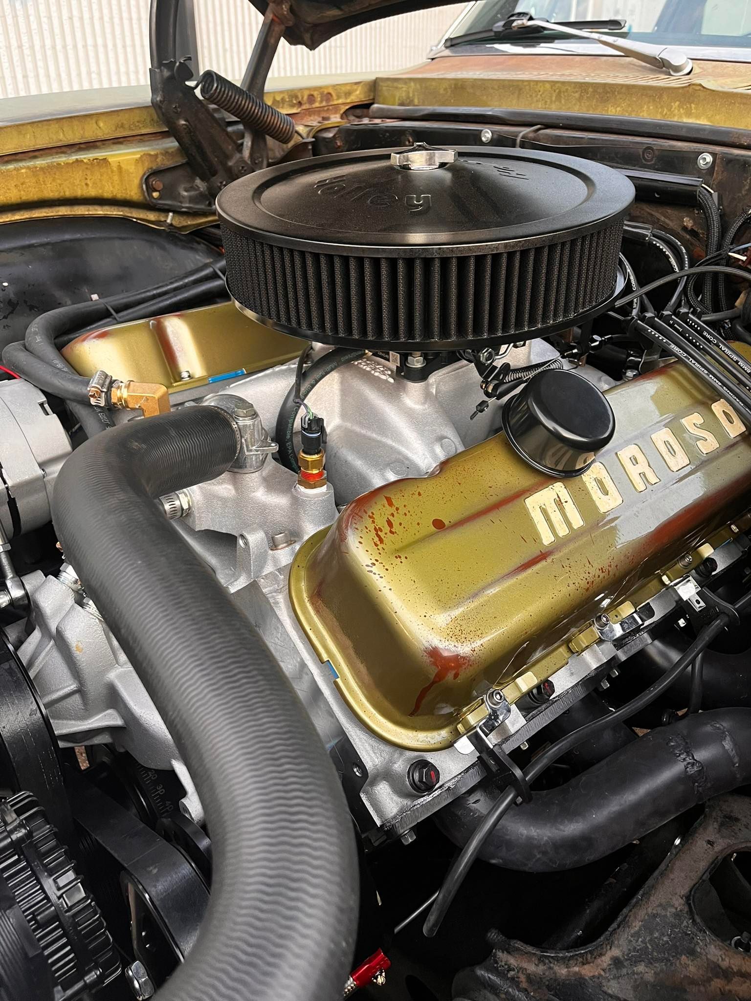 Close-up of a car engine with gold valve covers and a black air filter.