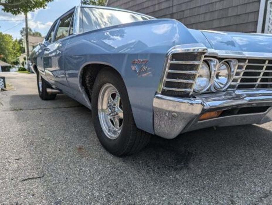 Light blue classic car parked on a paved driveway with chrome details and custom wheels.