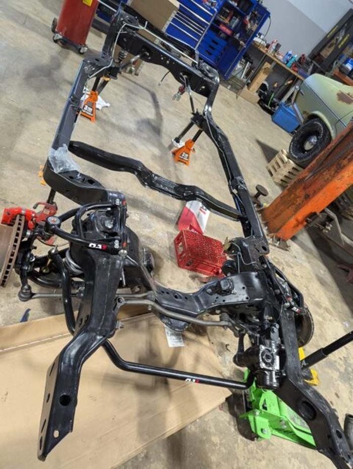 Black car chassis with suspension components in a garage setting.