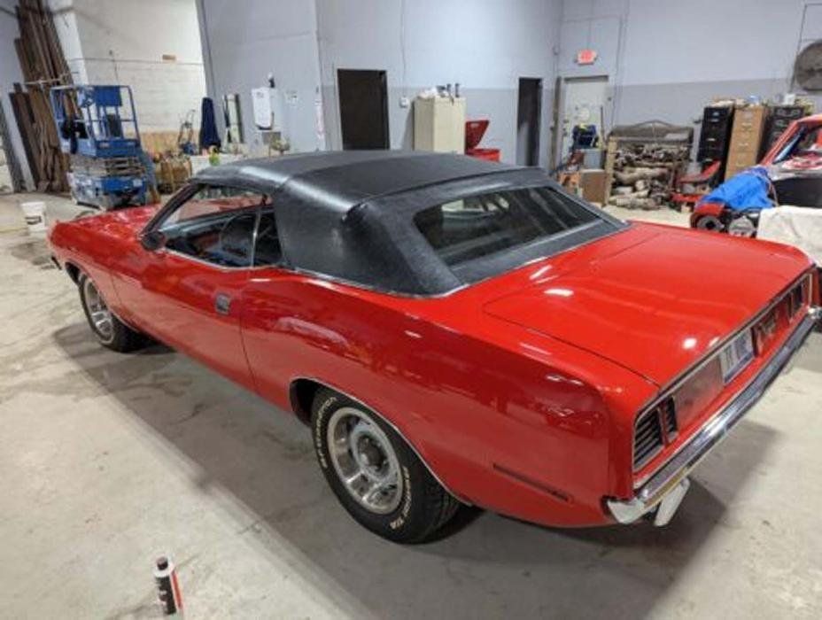 Red classic car with black top in a garage setting.