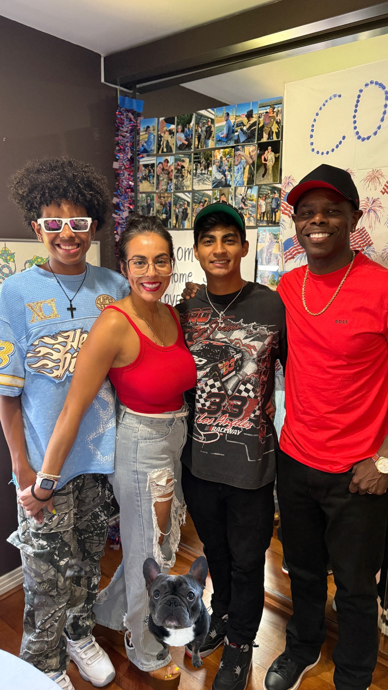 A group of four people and a dog posing indoors. Two men on either side, a woman in a red top, and a teen in the middle.