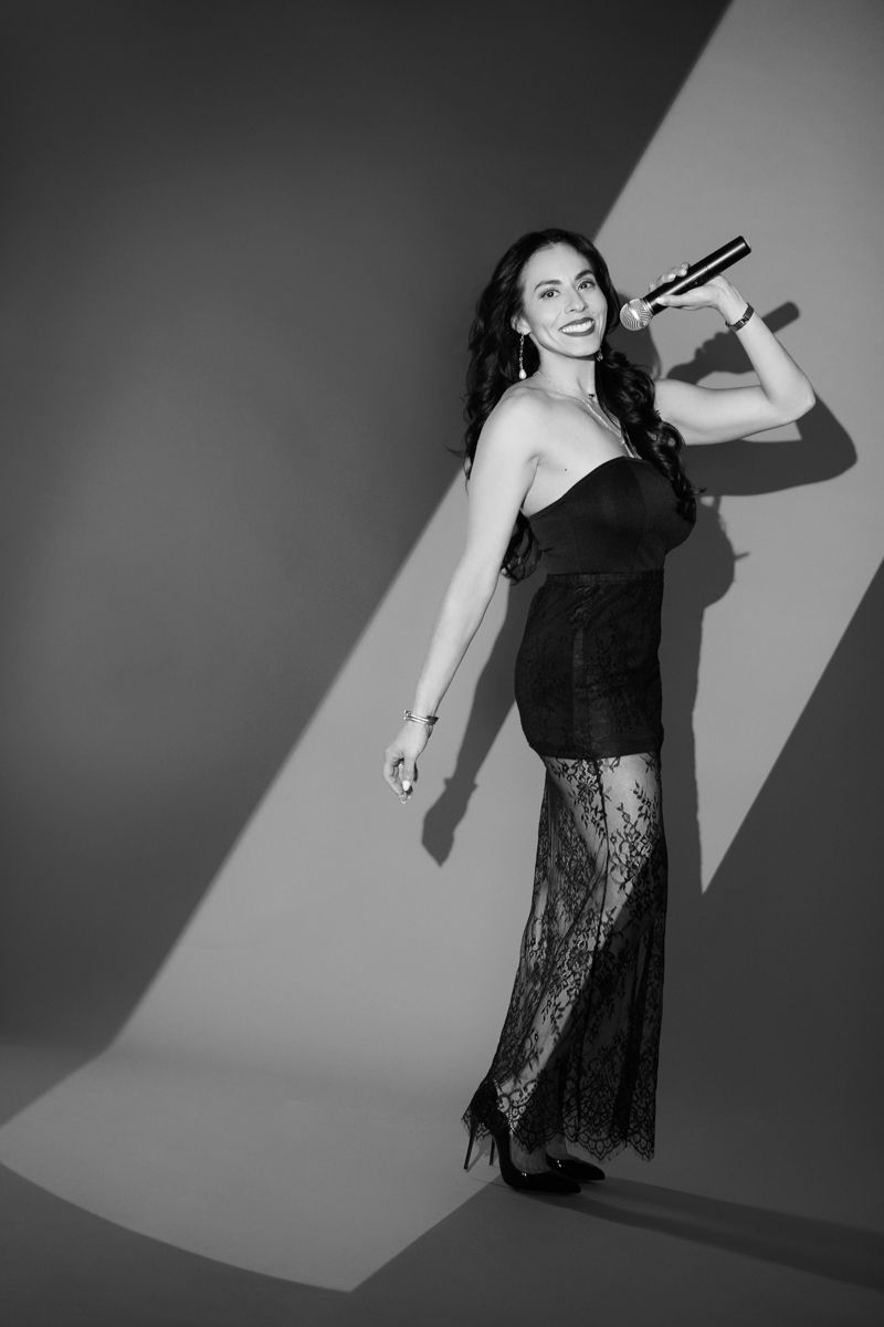 Woman in a black evening gown, smiling with hands on her hips, against a white background.