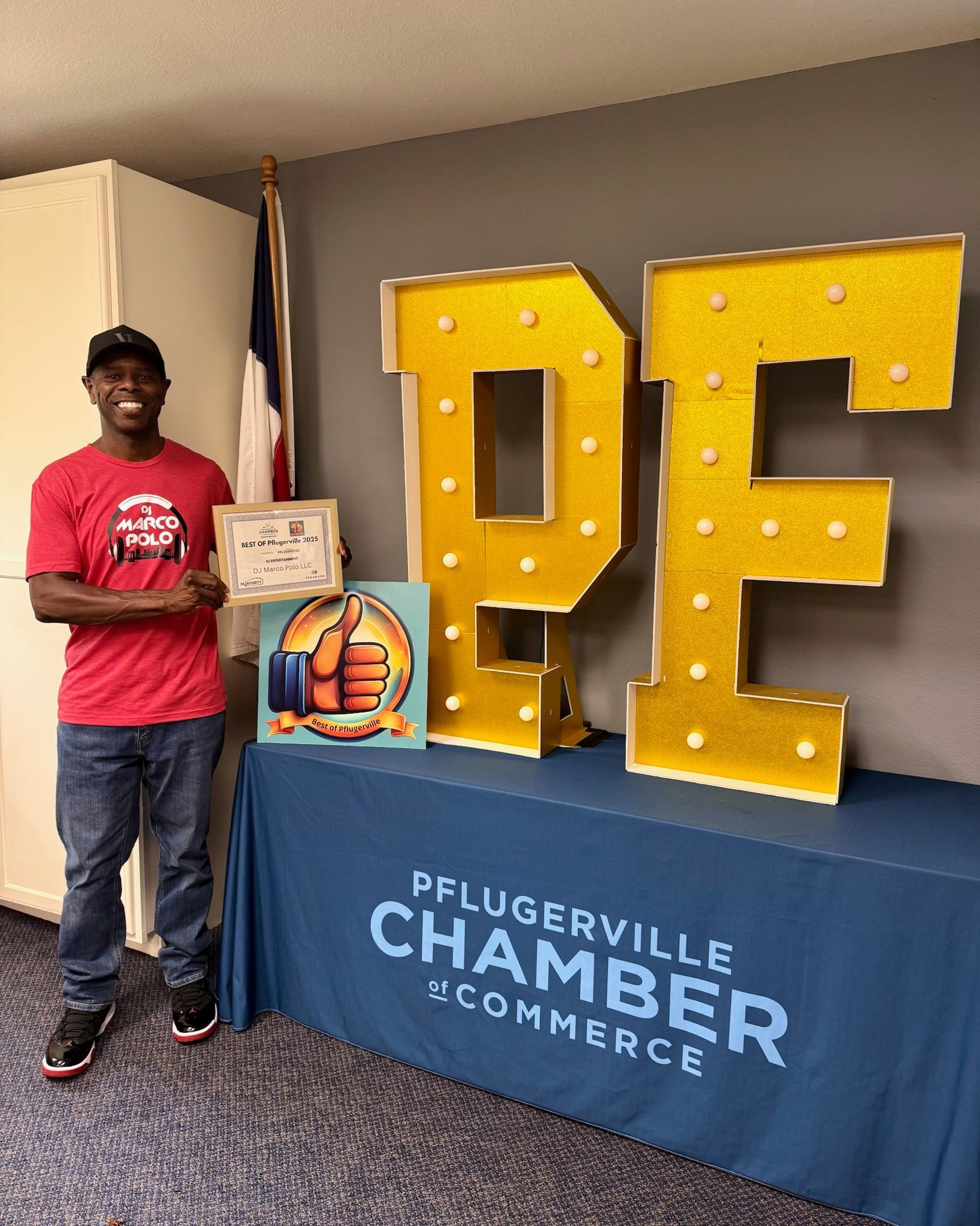 A man in a red shirt smiles, holding an award next to giant light-up
