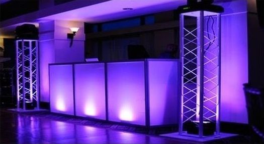 Purple-lit DJ setup with two truss towers and a white-paneled booth, likely at an event or party.
