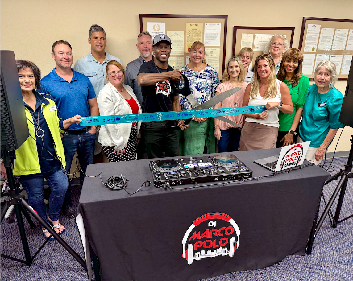 A group of people at a DJ setup, smiling while holding giant scissors for a ribbon-cutting ceremony.