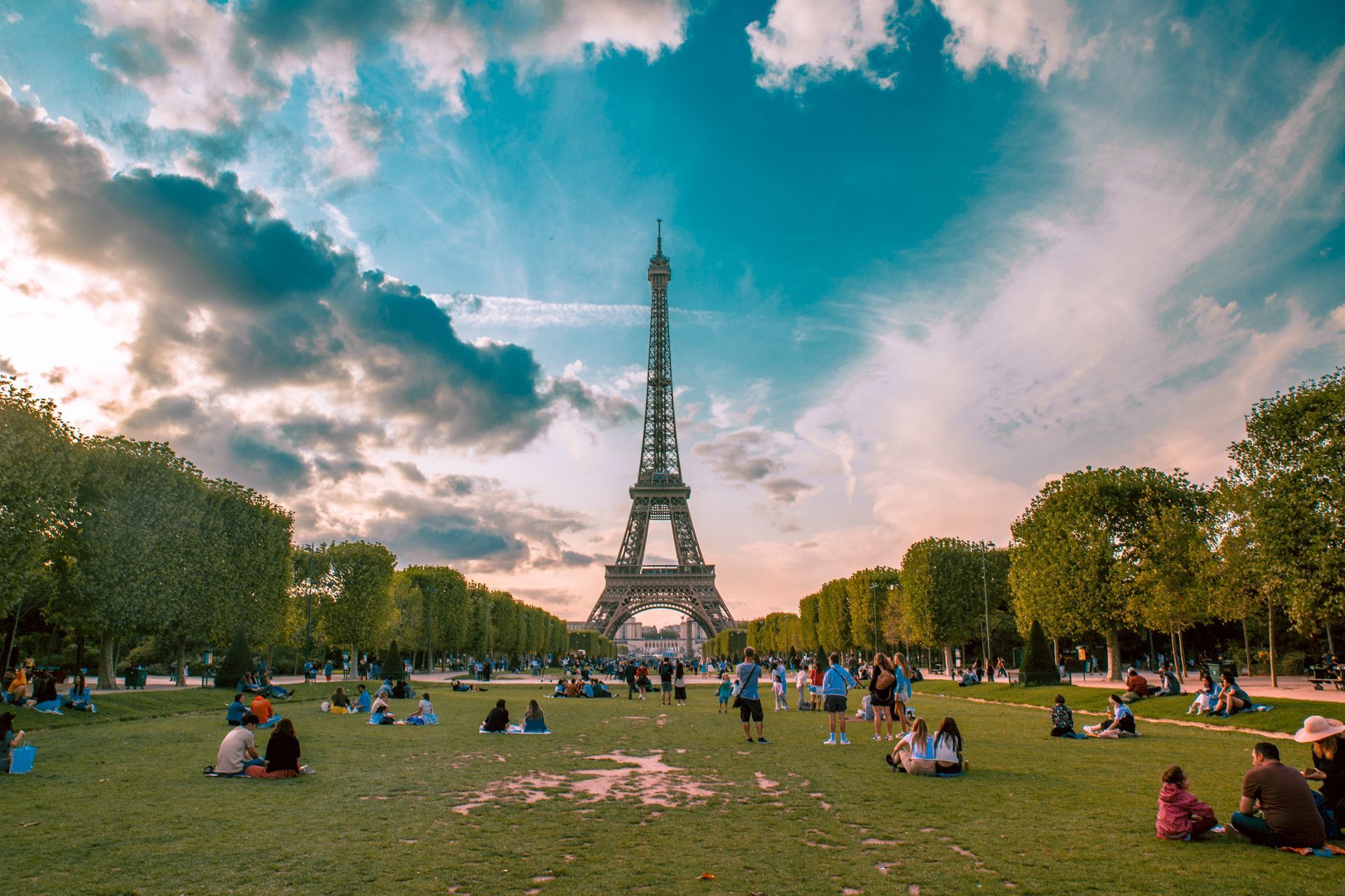 A group of people are sitting in a park in front of the eiffel tower.