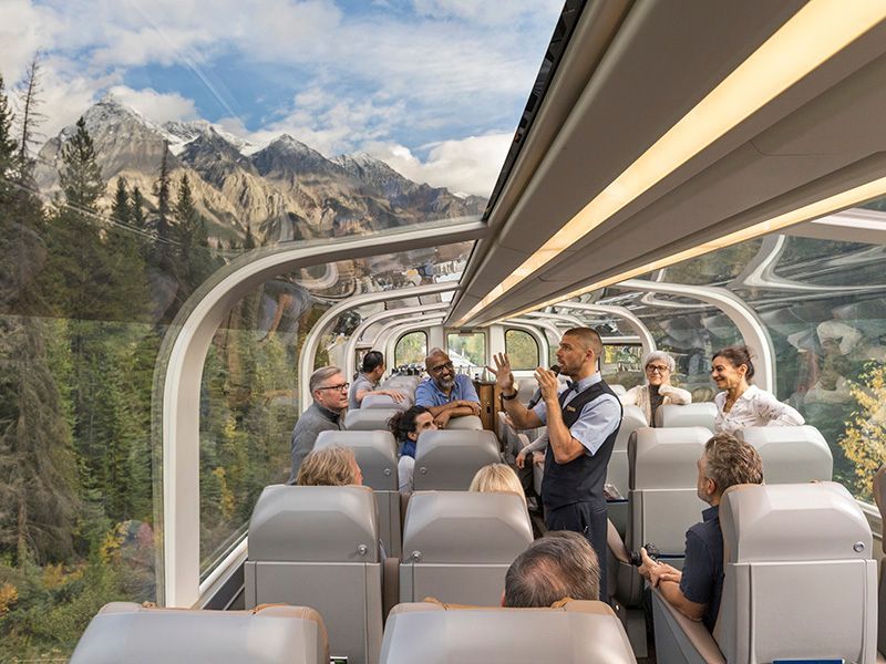 A group of people are sitting on a train with mountains in the background.