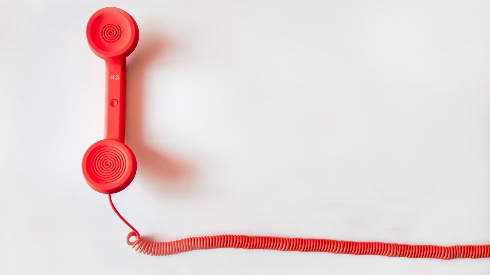 A red telephone with a red cord on a white background.