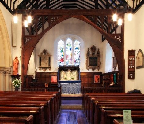 Inside a church: wooden pews, large arched window, sunlight streams in, clock on wall, and light wood ceiling.