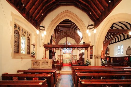 Choir performing in a church with stained glass window, red carpet, and attendees in pews.