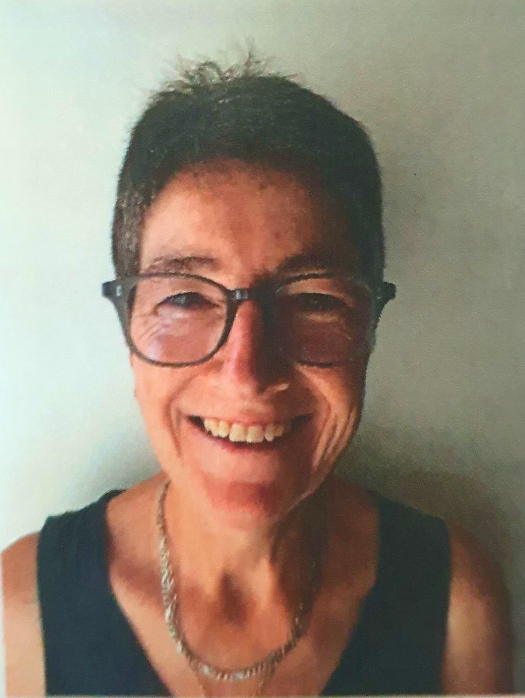 Woman with short dark hair, glasses, smiling, wearing a black top and silver necklace.