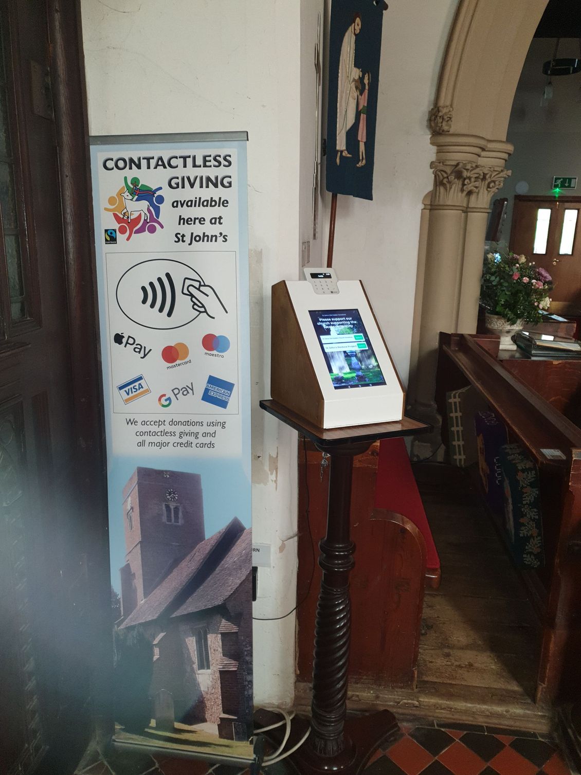 A contactless giving station in a church. Signage and a digital display on a stand.
