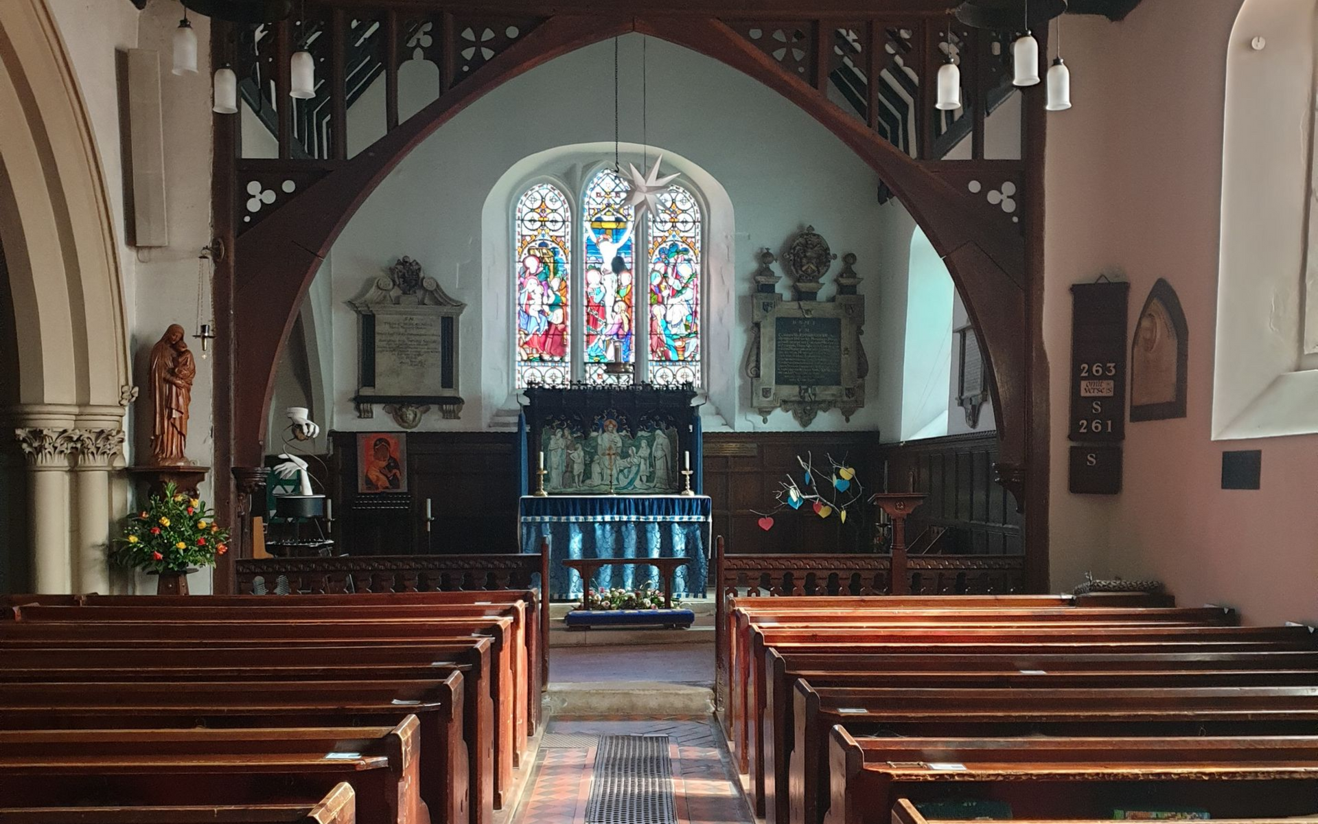 Interior of a church with wooden pews, stained glass window, and a wooden archway.