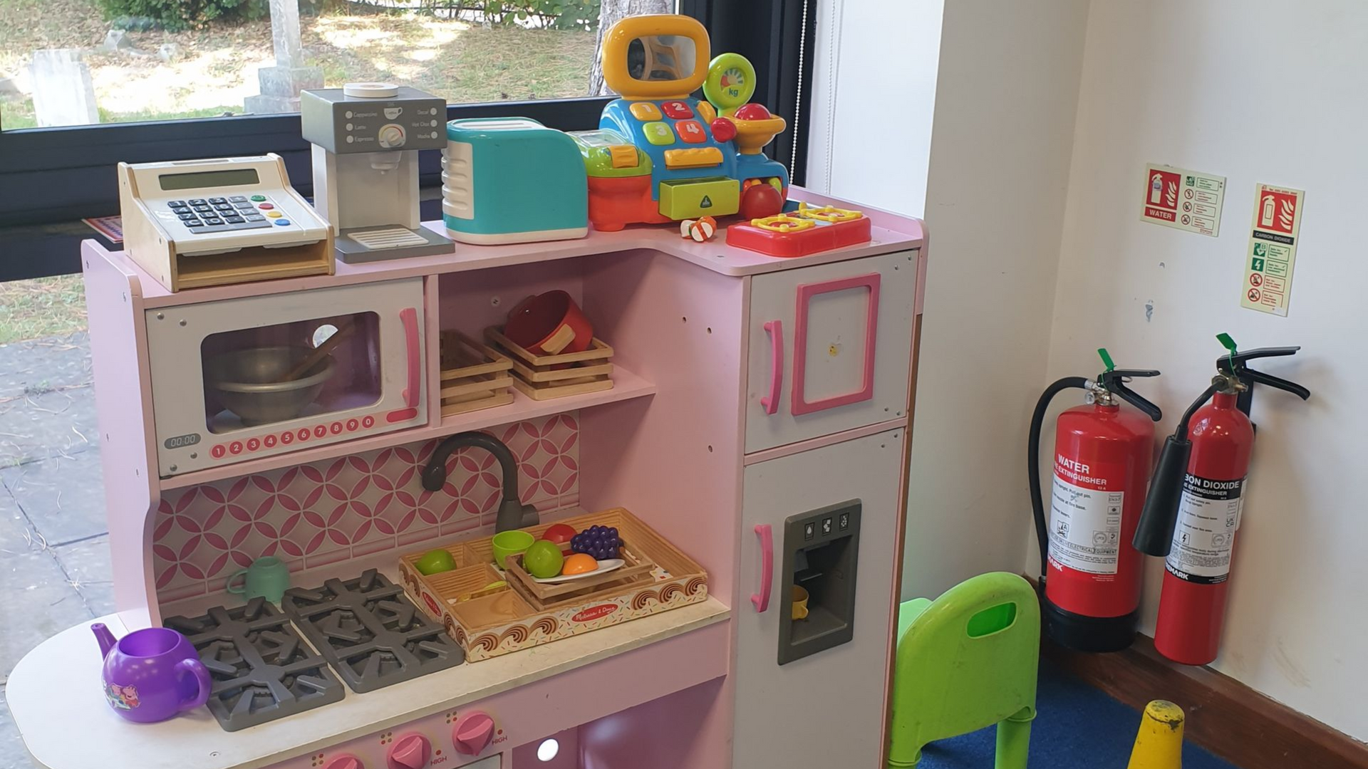 Child's pink play kitchen with toy appliances and fire extinguishers nearby.