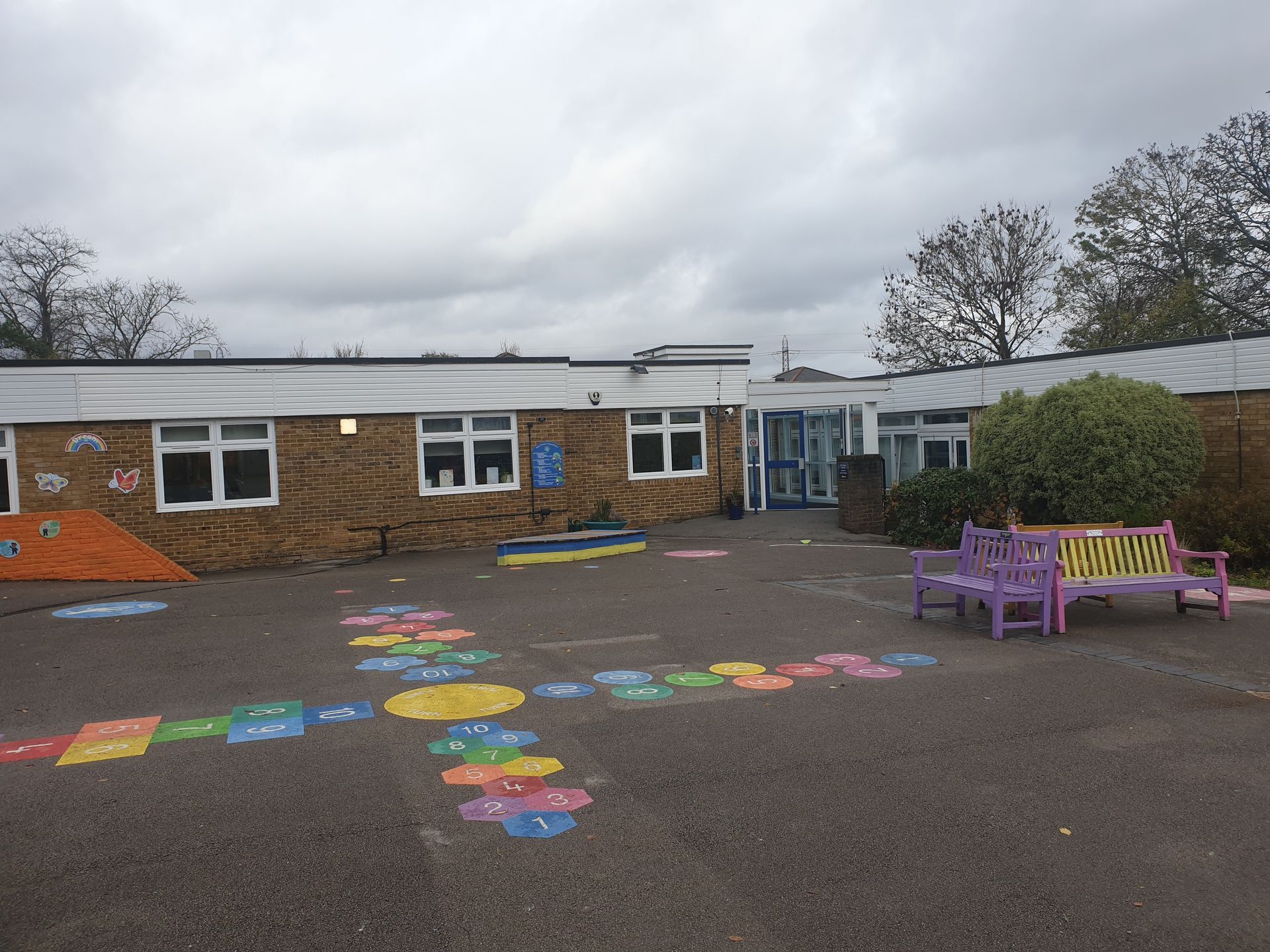 Schoolyard with hopscotch, colorful benches, and a building under a cloudy sky.