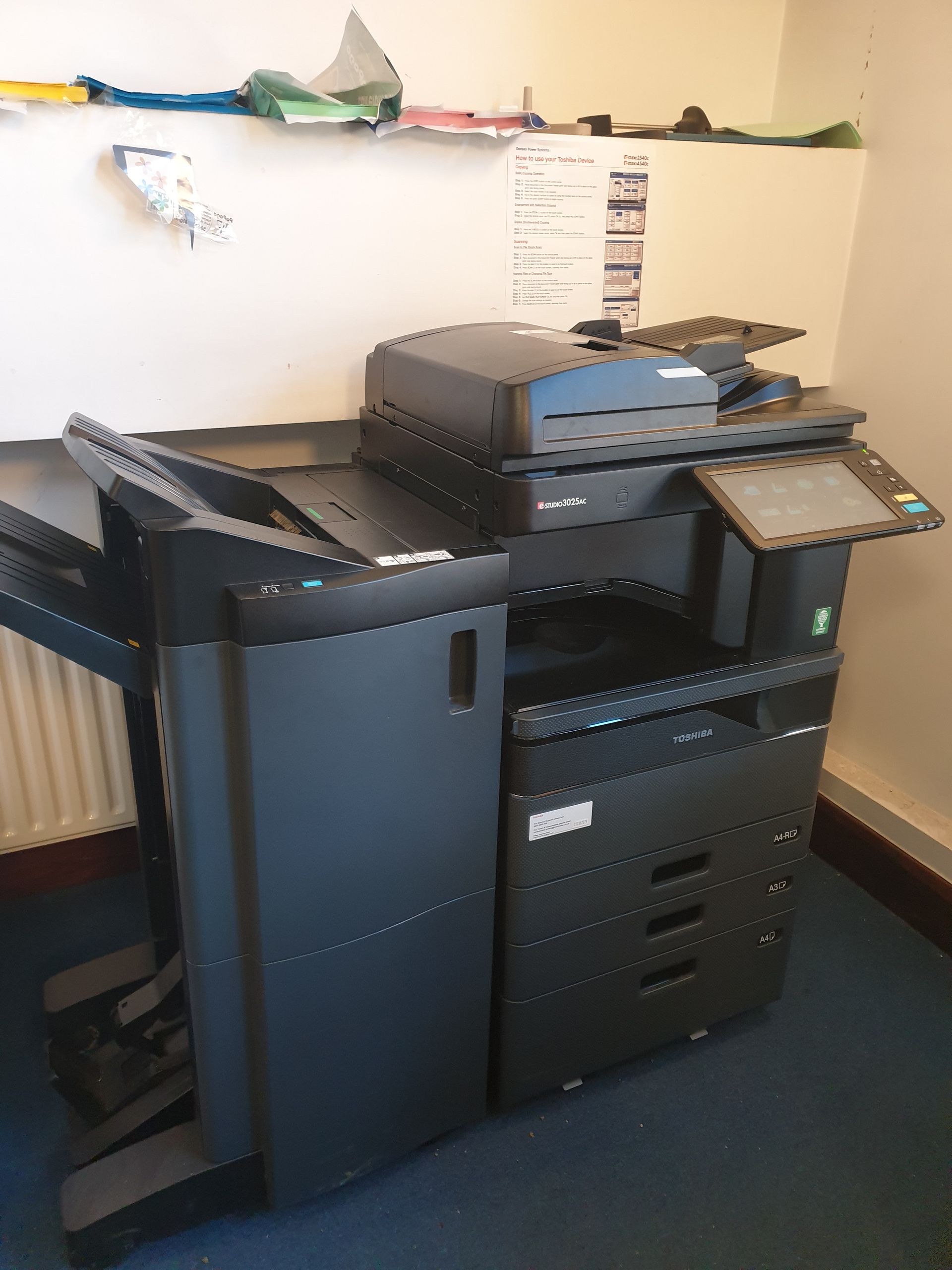 Black office copier with touch screen, paper trays, and document feeder.