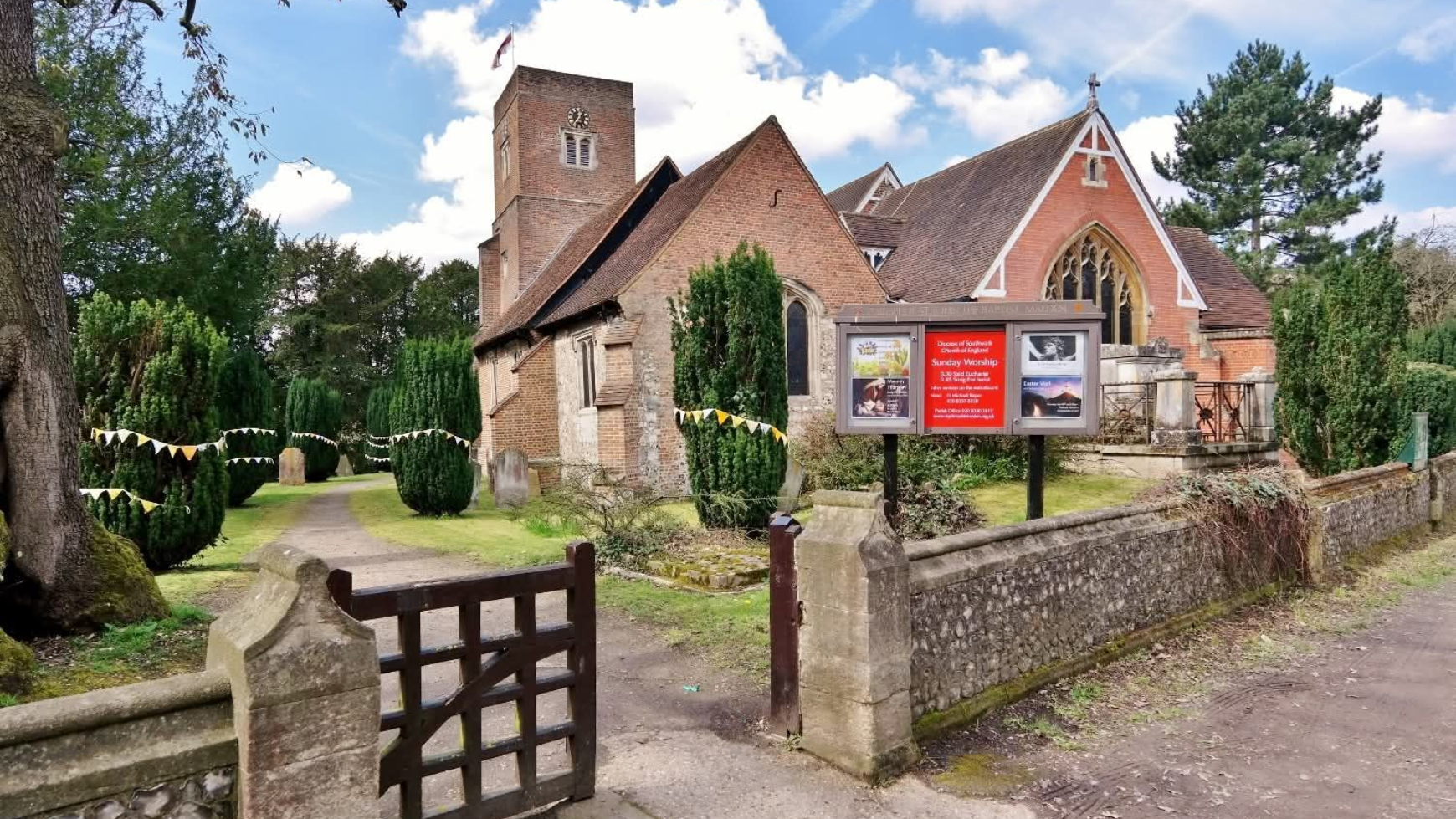 Church building with red brick roof, stone walls, and wooden gate.