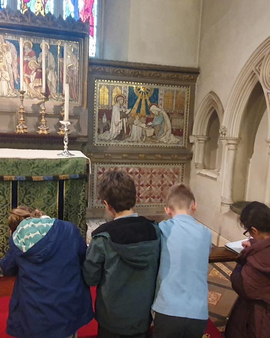 Children kneeling at an altar in a church, observing a religious artwork.