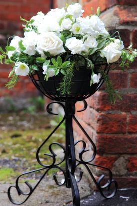 White flowers in a black, decorative plant stand against a red brick wall.