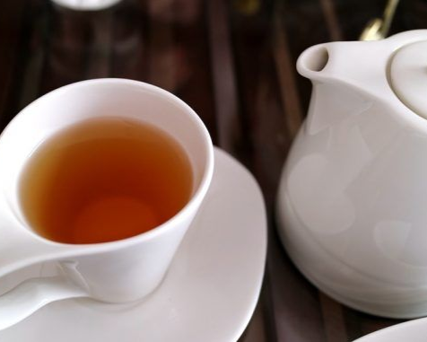 White teacup with tea and matching teapot on a saucer, on a dark wooden surface.