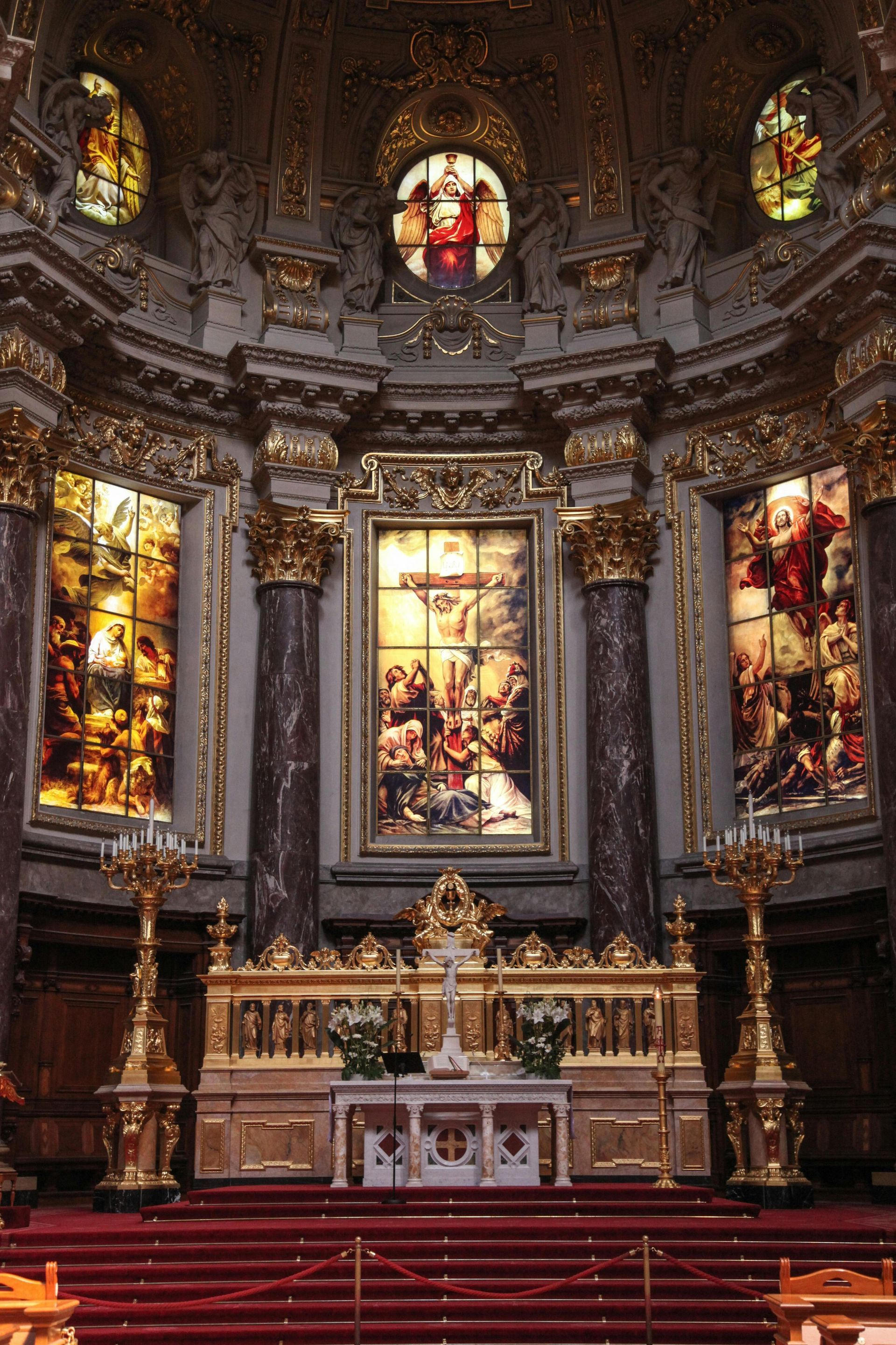 Interior view of a church altar with stained glass windows, a large painting, and gold accents.